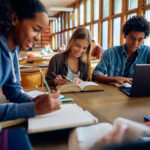 Group of happy classmates studying together at high school library.